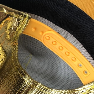 Détail de la texture serpent dorée et de la fermeture snapback orange de la casquette