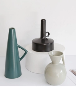 Three Nordic ceramic vases in matte green, black, and beige with geometric handles