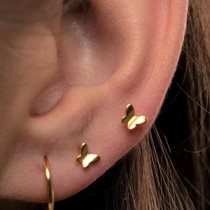 Elegant gold butterfly stud earrings and small hoop set on model's ear for stylish look