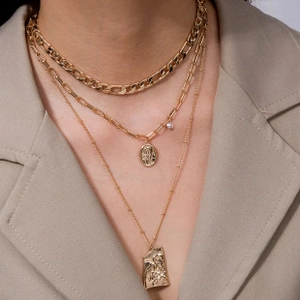 Close-up of layered gold necklace with pearl and rectangular vintage figure pendants