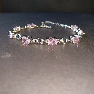 Detail of silver link bracelet with oval pink crystals and lobster clasp on dark background