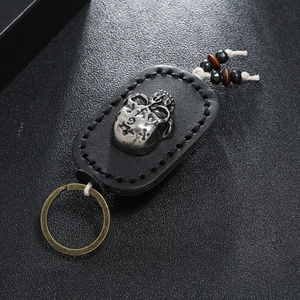 Detail view of a skull keychain with black stitched leather and vintage wood beads