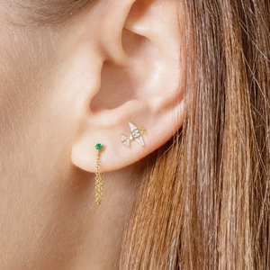 Gold airplane stud earrings with zircons and green gemstone chain dangle on model's ear
