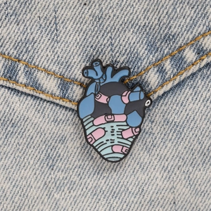 Macro detail of anatomical heart enamel pin on denim fabric with pill patterns