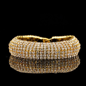 Detailed close-up of a sparkling gold bracelet with clear rhinestones on a black background