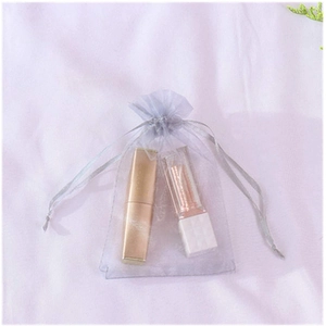 Detail of purple organza gift bag with drawstring showing cosmetics inside against silk fabric