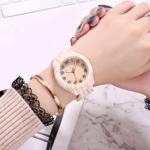 Detail of wooden watch with bamboo grain and numeric dial on wrist with gold bracelet