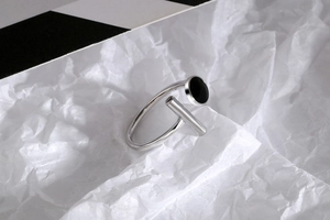 Macro shot of silver open ring with black enamel circular detail on textured background