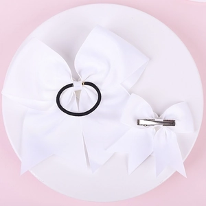 Detail view of large and small white bows with elastic hair tie and metal clip on a plate