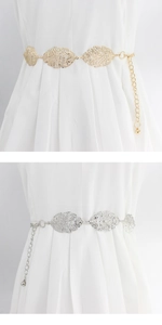 Detail of leaf-shaped metal waist chains in gold and silver on a pleated white dress