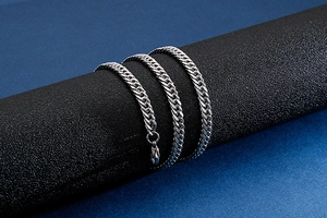 Detail of silver Cuban link necklace with lobster clasp on a black textured stand