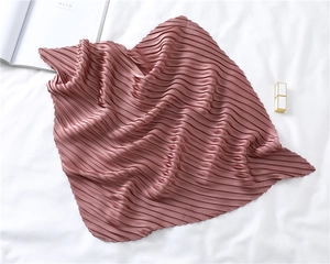 Detail of light pink pleated silk scarf displayed with magazine and lipstick props