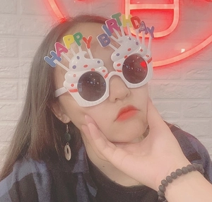 Close-up of a woman wearing white Happy Birthday party sunglasses with colorful letters