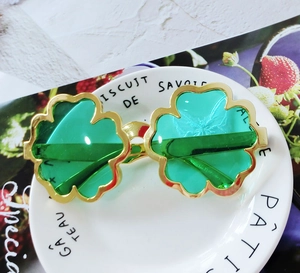 Detail of green four-leaf clover party sunglasses with golden metal frame on white plate