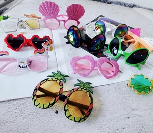 Flat lay of colorful novelty party sunglasses in pineapple and shell shapes on a table