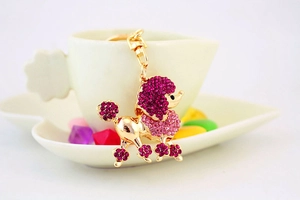 Detail view of a golden poodle keychain with pink and purple rhinestones on a ceramic dish