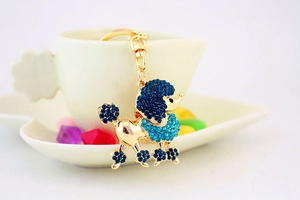 Close-up of golden poodle keychain with sparkling dark blue crystals hanging over white teacup
