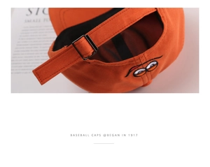 Detail of adjustable metal buckle and cartoon eye embroidery on orange cotton baseball cap