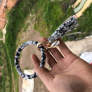 Detail of a snake print PU leather bangle keychain with a black and white tassel and gold ring