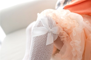 Close-up of white mesh knee-high baby socks featuring a large satin bow decoration