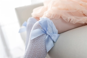 Detail of white mesh baby socks with a light blue satin bow and breathable hollow-out texture