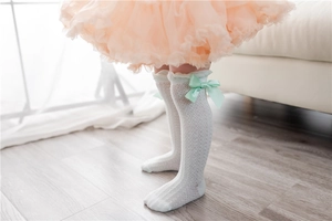 Detail of children's white mesh lace knee-high socks with light green satin bow decoration