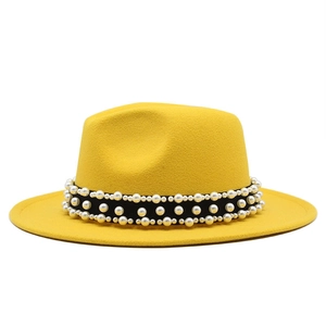 Détail d'un chapeau fedora jaune avec bande noire ornée de perles blanches élégantes