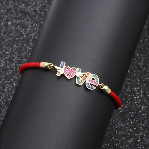 Close-up of red braided rope bracelet with colorful zircon stones on gold LOVE charm