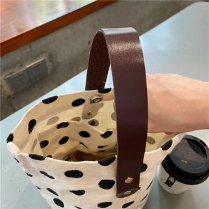 Detailed close-up of retro polka dot canvas bucket bag with brown leather handles and snap button