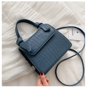 Detailed close-up of dark blue crocodile texture handbag on a soft white fabric surface