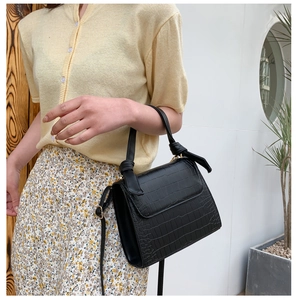 Detail of black crocodile texture handbag with knotted handle and adjustable strap