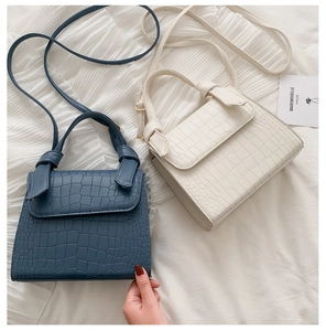 Detail of crocodile embossed crossbody bags in blue and white with knotted strap accents