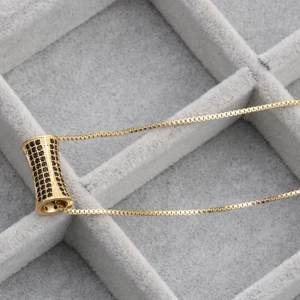 Gold plated necklace with micro-paved black zircon cylinder pendant on velvet tray