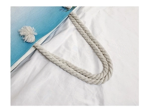 Close-up of a blue gradient woven beach tote bag with white cotton rope handles and pom-poms