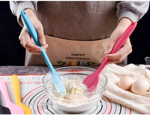 Close-up of blue and rose red silicone spatulas mixing ingredients in a glass bowl