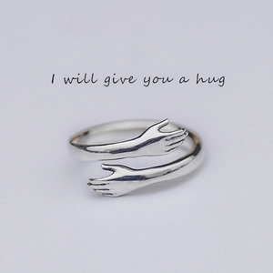 Macro detail of silver hugging hands ring featuring an adjustable open band design