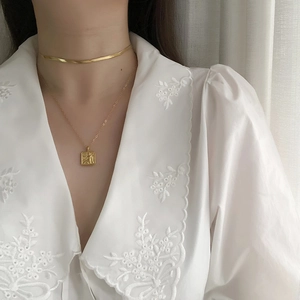 Detail of layered gold snake chain and vintage square pendant necklace on a model