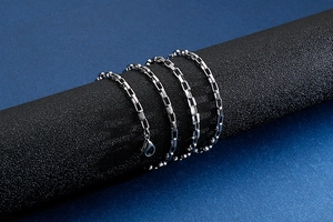 Close-up of a silver stainless steel box chain necklace on a black cylinder display