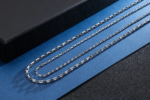Detail of silver box chain necklace on black gift box with a blue frosted background