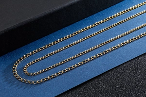 Macro detail of golden stainless steel flat chain links displayed on a black jewelry gift box