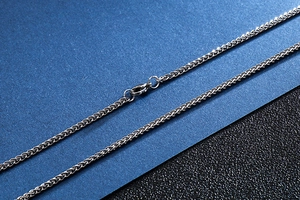 Detailed view of silver wheat chain necklace with lobster clasp on geometric background