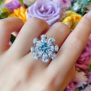 Close-up of a floral silver ring with a square blue gemstone worn on a finger