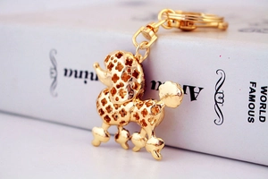 Golden poodle keychain with intricate floral hollow design leaning against a white book
