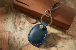 Close-up of a navy blue leather AirTag keychain holder with brass hardware on retro map