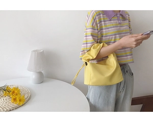 Sac baguette minimaliste en tissu jaune vif tenu par un mannequin en studio épuré