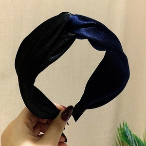 Detail of hand holding a black and blue satin knotted headband with vintage cross design