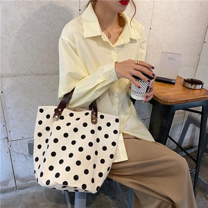 Close-up of black polka dot canvas tote bag with premium brown leather straps and rivets