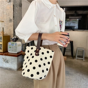 Polka dot canvas bucket bag with brown leather handles shown in a lifestyle cafe setting