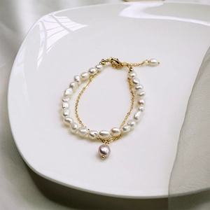 Détail d'un bracelet multicouche en perles baroques avec chaîne dorée et pendentif