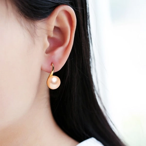 Elegant natural pink pearl drop earrings with gold fishhook on a model in soft light